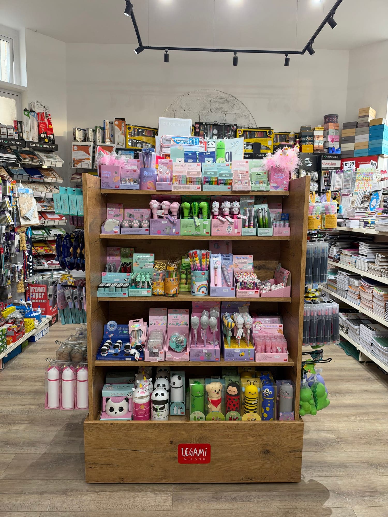 A Legami stand of fun stationery: animal-topped pens, novelty erasers, pencil cases and water bottles, with art supplies and paper on the shelves behind.