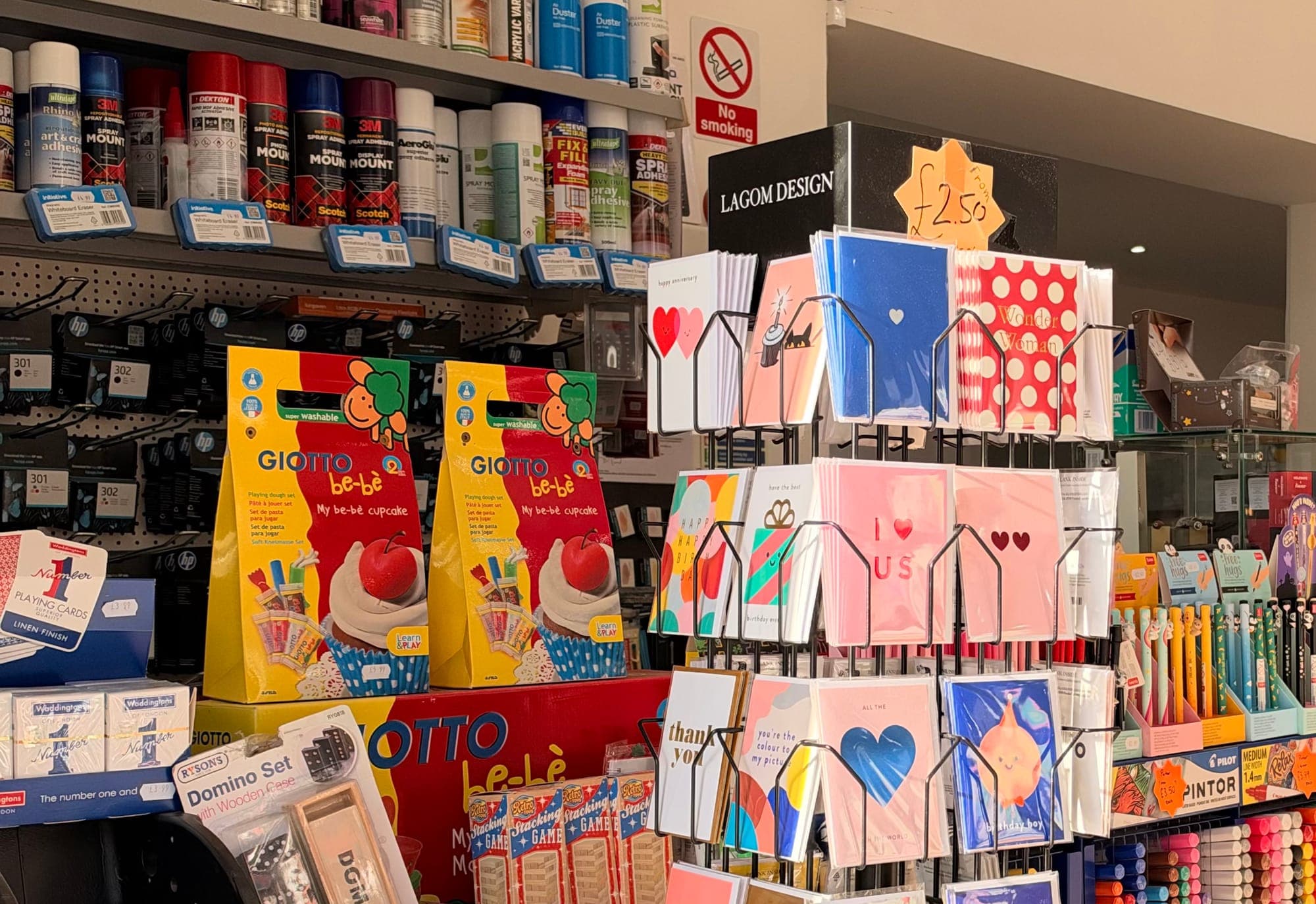 Inside the shop: a spinner of colourful greeting cards by the counter, with Giotto craft sets, spray adhesives and pens on the shelves