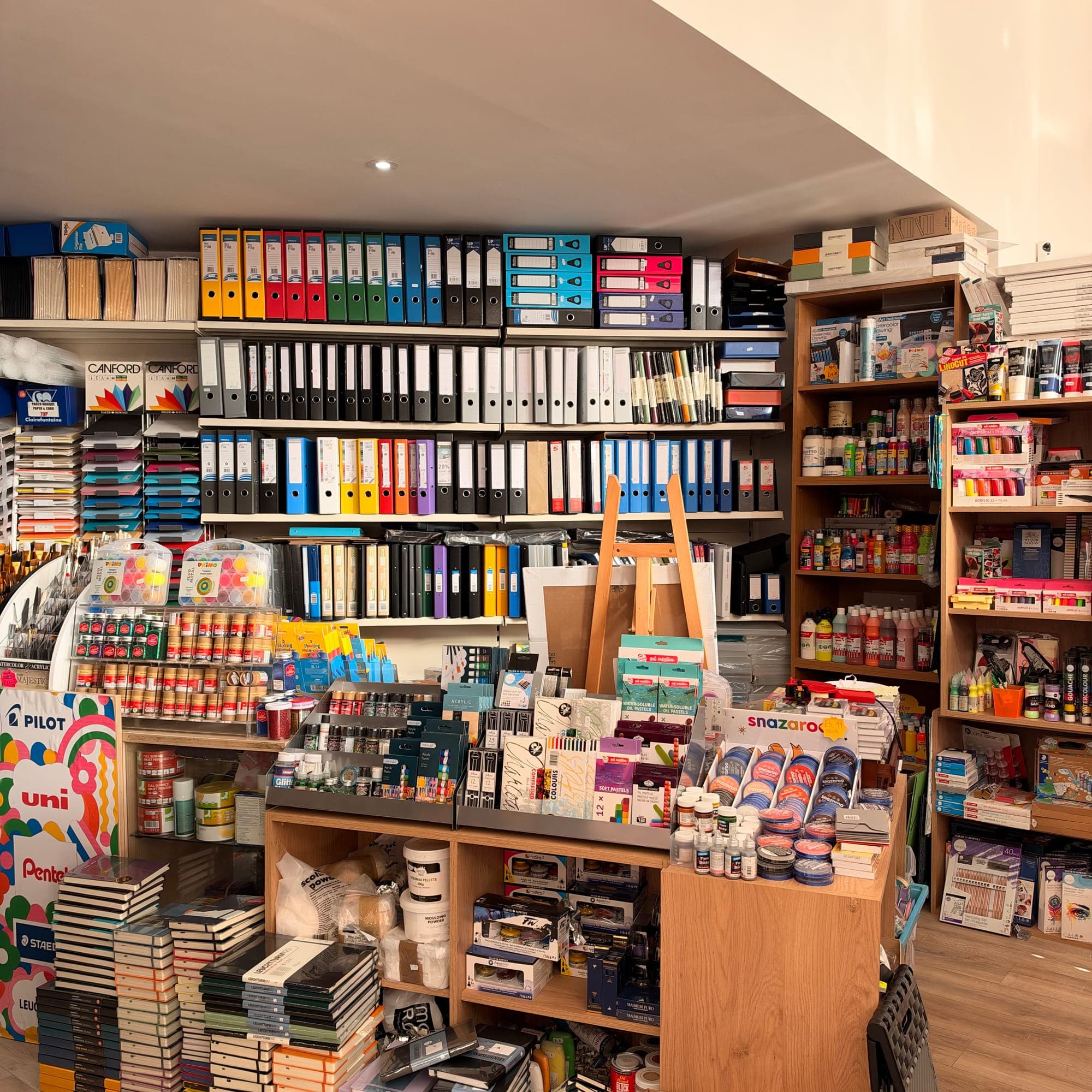 Shelves of box files, paints, art card and sketchbooks, with an easel on display